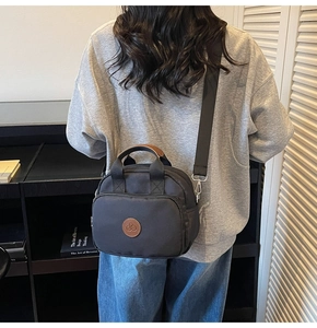 Detail of a black nylon crossbody bag with brown leather accents and wide shoulder strap