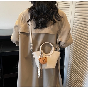 Elegante borsa a secchiello bianco crema con ciondolo a orsetto indossata su un trench kaki