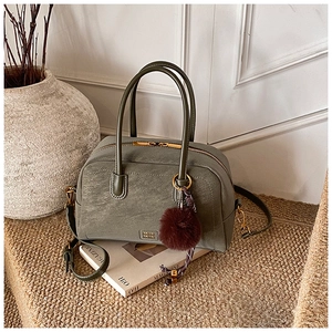 Detail view of olive green pillow bag with gold metal logo and brown fur pompom charm