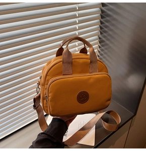 Detail of ginger yellow nylon crossbody bag featuring silver zippers and logo patch