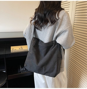 Detailed back view of a minimalist large capacity black canvas tote bag worn by a model