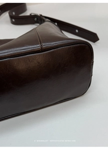 Detail of dark brown glossy leather crossbody bag with stitching and metal rivet strap