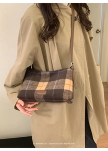 Detail of wool plaid tote bag with brown leather strap worn over a beige trench coat