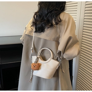 Dettaglio borsa a secchiello beige con manico in metallo, ciondolo orsetto e foulard a righe