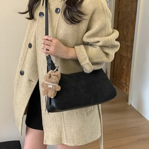 Detail of minimalist black dumpling shoulder bag with cute brown bear charm on the strap