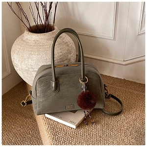 Detail of dark olive green boston bag with litchi texture and red fur ball ornament