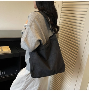 Large black canvas tote bag with wide shoulder strap shown on model for daily commute
