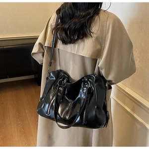 Vue détaillée d'un grand sac cabas noir en similicuir brillant porté avec un trench-coat