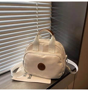 Detailed close-up of cream nylon crossbody bag with brown leather logo and light shadows