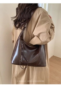 Detail of a large brown oil-wax leather tote bag with vertical zipper and long tassels