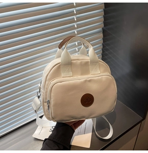Detail of a creamy white nylon backpack with a brown leather bike logo and zipper front pocket