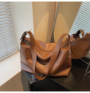 Detail of caramel brown leather tote bag showing wide shoulder strap and gold buckle
