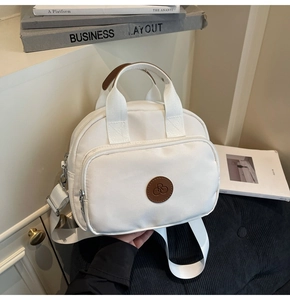 Close-up of minimalist white messenger bag with front zipper pocket and brown leather handle