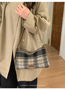 Detail of plaid wool tote bag with brown leather strap and brand tag on trench coat