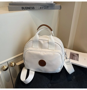 Detail view of white canvas crossbody bag with brown leather logo and adjustable strap