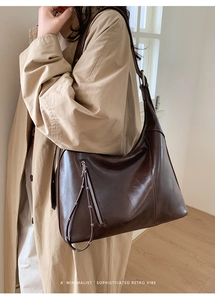 Detailed close-up of retro dark brown hobo bag with zipper and rivets on beige coat