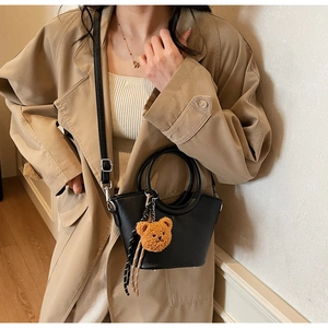 Borsa a secchiello in pelle nera con manico e ciondolo a orso su trench beige