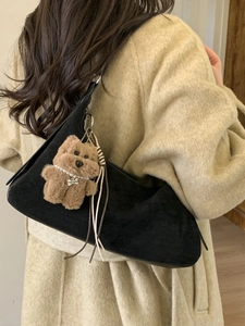 Minimalist black suede dumpling bag with plush bear charm and tassel detail on model