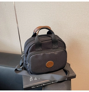 Detail of black nylon crossbody bag with brown leather handles on a decorative book