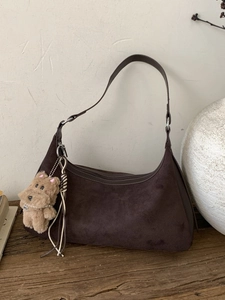 Deep brown suede hobo shoulder bag with plush puppy pendant on a rustic wooden desk