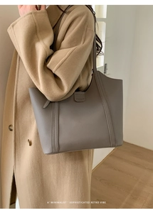 Détail d'un grand cabas en cuir gris mat avec sangle logo porté sur un manteau en laine