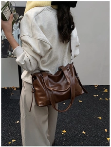 Detail of dark brown glossy leather tote bag with silver hardware on model's shoulder