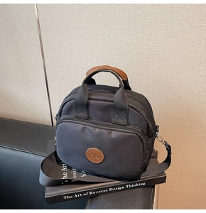 Detail of black crossbody bag with dual zippers and leather handle over art books