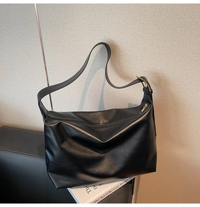 Close-up of matte black leather tote bag with gold zipper and wide shoulder strap detail
