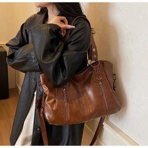 Détail du sac cabas vintage en cuir marron avec zips argentés porté sur un trench noir