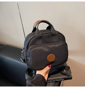 Detail view of the black crossbody bag showing dual zippers and brown leather logo patch