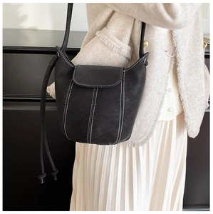 Detail of black leather bucket bag with white contrast stitching and magnetic flap closure