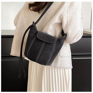 Detail of black bucket bag featuring white contrast stitching and elegant flap closure