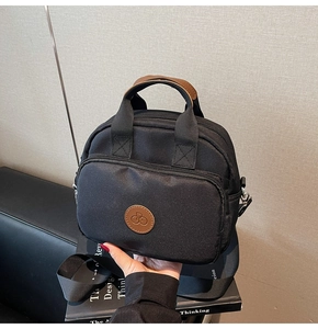 Detail of black nylon crossbody bag with brown leather logo and top padded handles