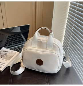 Detail of white nylon shoulder bag with brown leather logo patch and metal zipper