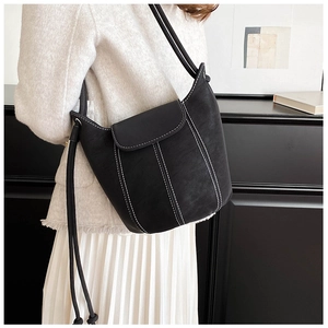 Detail of black leather bucket bag featuring contrast white stitching on a model's shoulder