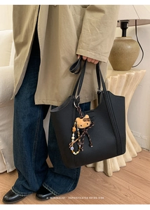 Détail d'un sac cabas en cuir grainé noir avec un pendentif peluche dans un décor épuré