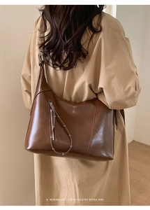 Detail view of brown glossy leather crossbody bag with minimalist retro vibe and tassel zip