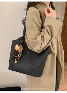 Détail du grand cabas en cuir grainé noir avec charme en peluche sur trench beige