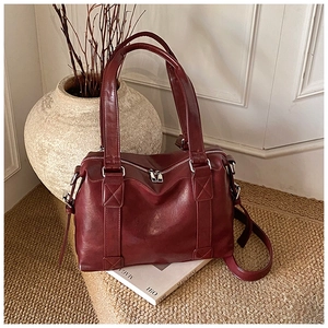 Detail of burgundy leather tote bag with silver hardware on a rustic textured surface