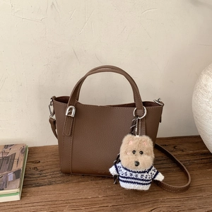 Detail of a dark brown pebble leather bucket bag with silver hardware and a cute bear charm