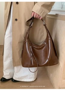Detail of dark brown oily faux leather hobo bag with vertical zipper and ring puller