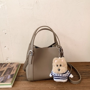 Detail of grey lychee leather bucket bag with a cute plush dog pendant on a wooden surface
