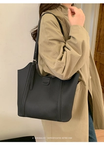 Gros plan sur un sac cabas en cuir grainé noir porté avec un trench-coat beige élégant
