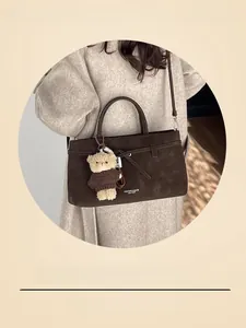 Detail of dark brown leather tote bag featuring a teddy bear charm and metal buckle strap