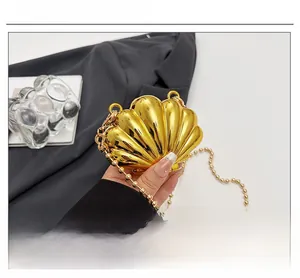 Detail of a polished gold shell clutch bag with a bead chain on mirror finish surface