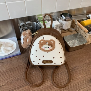 Detailed close-up of white polka dot backpack featuring plush bear embroidery and charm