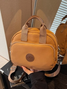 Brown nylon crossbody bag with dual handles and wide adjustable strap in life scene