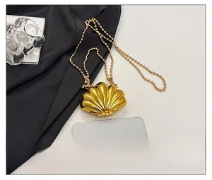 Miniature gold shell chain bag shown next to a smartphone for a size comparison
