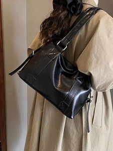 Large black PU leather tote bag with wide strap on a model in a khaki trench coat