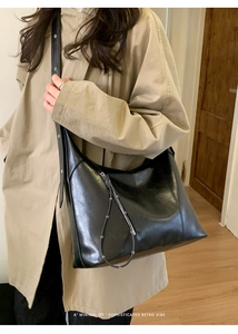 Detail of minimalist black leather shoulder bag with diagonal zipper and metal buckle strap